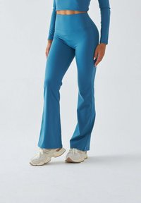 Sportowy strój w kolorze morskim, składający się z krótkiego topu z długimi rękawami oraz wysokich, rozszerzanych legginsów. Materiał jest gładki i elastyczny.