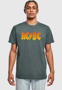 T-paita tummanharmaasta puuvillasta, jossa on bändin nimi "AC/DC" vahvassa oranssissa kirjasimessa salama-akkentilla, lyhyet hihat ja pyöreä pääntie.