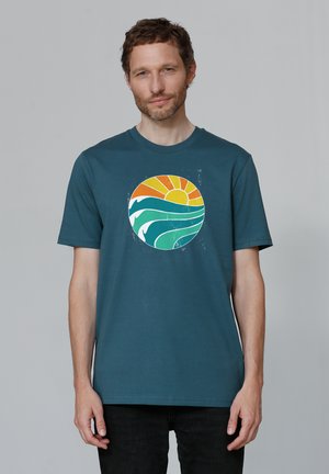 Teal katoenen t-shirt met een cirkelvormige grafiek van golven en een zon in oranje en gele tinten, met een ontspannen pasvorm en korte mouwen.