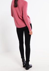 Pink knit sweater with a relaxed fit, paired with black skinny pants and black ankle boots. Smooth texture and seamless design.