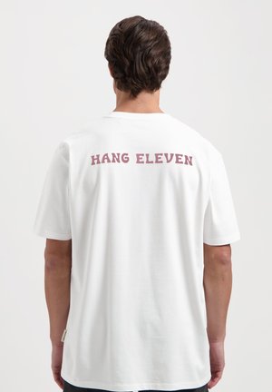Weißes Baumwoll-T-Shirt mit kurzen Ärmeln, auf dem Rücken mit "HANG ELEVEN" in Kastanienbraun bedruckt. Glatte Textur, lässige Passform.