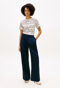 Λευκό μπλουζάκι με σχέδιο από αφηρημένες γραμμές, συνδυασμένο με ψηλόμεσο σκούρο μπλε παντελόνι με φαρδύ πόδι, με θηλιά ζώνης και πιέτες στο εμπρός μέρος.