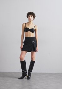 Bralet din paiete negre, fustă neagră cu talie înaltă și accent argintiu, și cizme negre lucioase până la genunchi. Textură netedă cu un design ajustat.