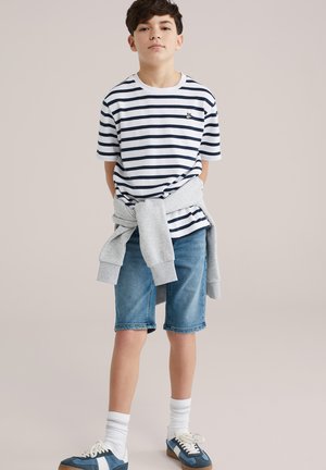 Striped short-sleeve t-shirt in white and navy; gray sweatshirt tied around waist; denim shorts; blue sneakers with white accents; white socks.