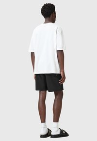 Camiseta blanca de manga corta combinada con pantalones cortos negros. Los pantalones cortos tienen un bolsillo lateral y están hechos de un tejido suave y ligero. Sandalias negras con tiras.