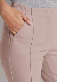 Helle rosa maßgeschneiderte Hose mit glattem Stofffinish, ausgestattet mit seitlichen Taschen, einer Knopfschließe und subtilen Stichdetails.