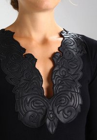 Top in maglia nera con profondo scollo a V decorato con ricami in pelle nera a rilievo a motivo vorticoso.