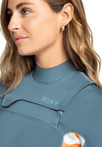 Wetsuit in muted teal with contrasting maroon stitch detail. Features a Roxy logo and a colorful pattern on the sleeve. High-neck design.