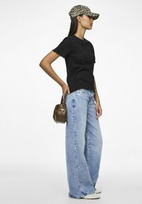 Svart ribbestrikket topp med korte ermer og bølgekant, lyseblå vide jeans, og en brun håndveske. Leopardmønstrete caps med buet skjerm er synlig.