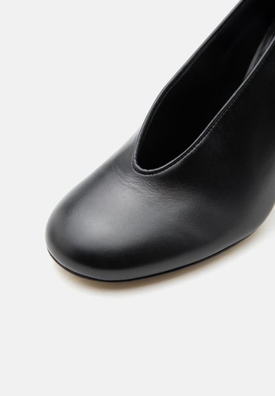 Μαύρο λείο δερμάτινο παπούτσι χωρίς κορδόνια με στρογγυλεμένη μύτη και χαμηλή γραμμή πέλματος σε λευκό φόντο.