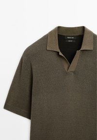 Kortærmet, grønbrown strikket polo shirt med et tekstureret mønster og en kontrastkrave. Har v-hals og subtile ribbede kanter.