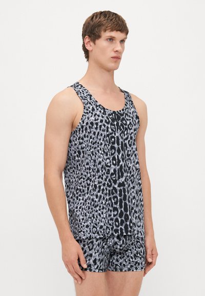 Junger Mann steht, trägt ein graues und schwarzes Leopardenmuster-Top und passende Boxershorts, schlichter heller Hintergrund.