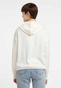Witte hoodie met een ontspannen ontwerp, voorzien van een grote capuchon en geribbelde manchetten. G gedragen met lichtblauwe high-waisted jeans en een gladde textuur.
