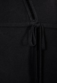 Tissu tricoté noir avec une fermeture éclair frontale et un cordon de serrage noué à la taille, montrant les détails de texture et de couture.