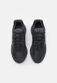 Čierne športové tenisky vyrobené z materiálov mesh a semišu. Medzi vlastnosti patrí okrúhly šnurovací systém, textúrované panely a odpružená podrážka.