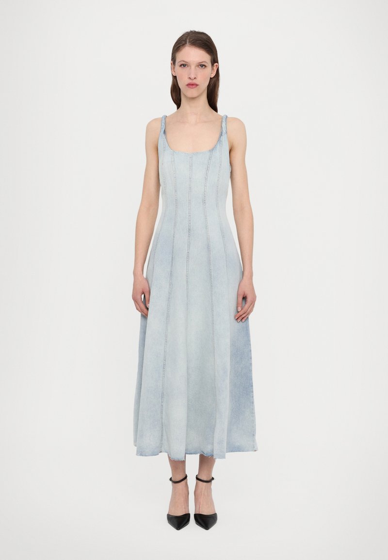 Helles, blaues Denim-Kleid mit tailliertem Oberteil und A-Linien-Rock, ausgestattet mit schmalen Trägern und sichtbaren Nahtdetails. Schwarze spitze Schuhe.