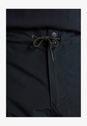 Shorts noirs avec une taille élastique à cordon de serrage, présentant une texture lisse et une fermeture à bouton. Le cordon de serrage est dans un design tressé contrastant.