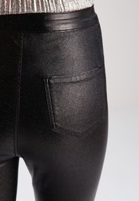Svarta metalliska leggings med en glansig finish, med en ficka baktill. Slät textur och slim-fit design.