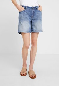 Vaaleansiniset farkkushortsit, joissa on kulutettua tyyliä. Ominaisuuksia ovat klassinen viiden taskun muotoilu, vetoketjupidennys ja viimeistelty helma.