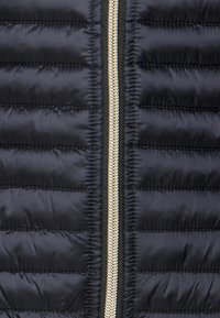 Black puffer jacket featuring horizontal quilted sections, a gold zipper, and a black zipper tape along the front opening. Smooth texture.