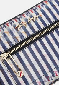 Gennemsigtig clutchtaske med et geometrisk mønster i blå, hvid og rød. Har hardware i guldtone og en sort lynlås.