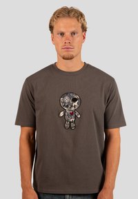 Šedé tričko s krátkým rukávem s texturovaným vyšívaným designem panenky se srdcem, umístěné na jednolitém pozadí.