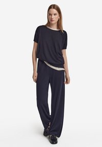 Granatowy, oversize'owy t-shirt z krótkim rękawem, noszony na jasnym topie, w połączeniu z szerokimi spodniami z bocznymi rozcięciami i czarnymi butami.