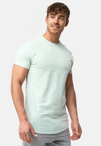 Minzgrünes T-Shirt mit kurzen Ärmeln aus weichem Stoff. Rundhalsausschnitt; dezentes Logo auf der Brust; gerade geschnittene Saumlinie; minimalistisches Design.