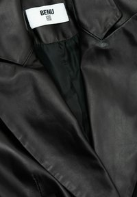 Czarna skórzana kurtka z czarną podszewką z tkaniny oraz biała metka wewnątrz z nazwą marki „BENU”.