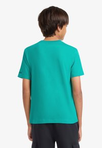 Τιρκουάζ κοντομάνικη μπλούζα από βαμβάκι. Διαθέτει απλό σχέδιο με στρογγυλή λαιμόκοψη. Λογότυπο στο αριστερό μανίκι. Μπορεί να συνδυαστεί με casual παντελόνια ή φούστες.