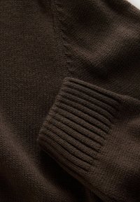 Brązowy sweter dziergany, z fakturowaną powierzchnią, ściągaczami i detalami szwów na ramionach. Miękki, ciepły materiał.