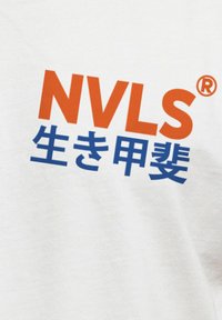 Weißes T-Shirt mit kräftigem orange und blauen Text: "NVLS" und "生き甲斐" (Bedeutung: "Ikigai"). Der Text ist modern und im grafischen Stil präsentiert.