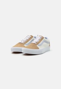 Sneakers met een tan suède bovenkant, witte leren accenten en witte veters. Dikke witte rubberen zool met textuur, low-top ontwerp.