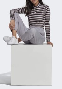 Prúžkovaná blúzka s dlhým rukávom v odtieňoch bielej a fialovej, skombinovaná s svetlosivými teplákmi. Biele tenisky dotvárajú outfit.