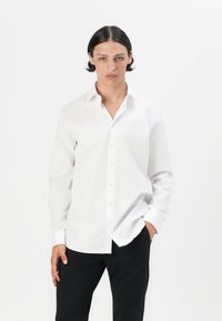 White button-up shirt with a collar, long sleeves, and a relaxed fit, paired with black trousers. Smooth texture, minimal design.