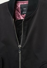 Veste bomber noire à extérieur lisse, fermeture éclair avant, col côtelé et doublure matelassée rose, présentant un design minimaliste et des accessoires métalliques.