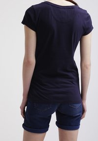 Námořnická modrá tričko s krátkým rukávem a kulatým výstřihem; nošené s ohrnutými džínovými šortkami s kapsami na zadní straně a hladkou texturou.