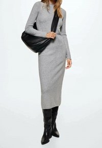 Robe en mélange de laine grise avec des manches longues, silhouette ajustée et coupe au genou. Associée à un sac fourre-tout noir et des bottes hautes.