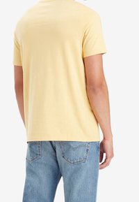 Koszulka z krótkim rękawem w żółtym kolorze, wykonana z bawełny, charakteryzująca się luźnym krojem. Noszona z niebieskimi dżinsami, prezentująca prosty design bez widocznych logo.
