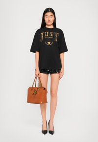 Black oversized t-shirt with gold print, shiny black shorts, brown handbag with chain straps, and pointed black shoes. Simple, modern style.