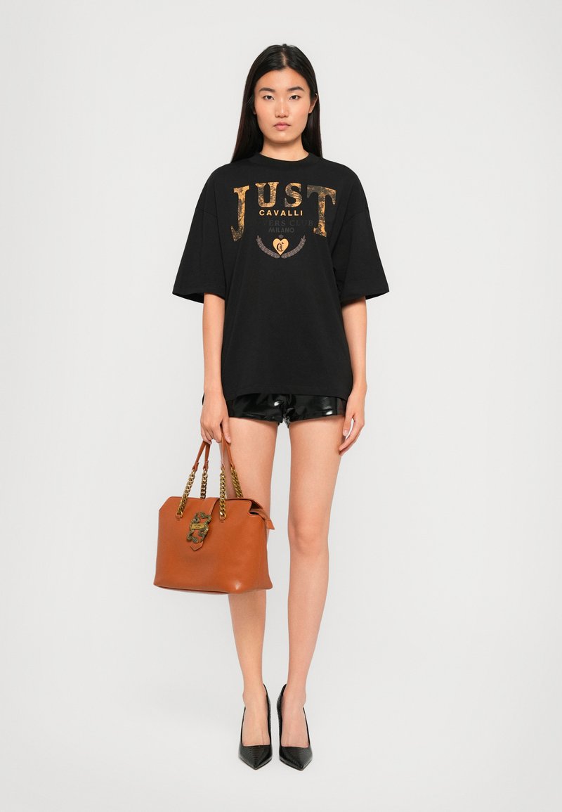 Black oversized t-shirt with gold print, shiny black shorts, brown handbag with chain straps, and pointed black shoes. Simple, modern style.