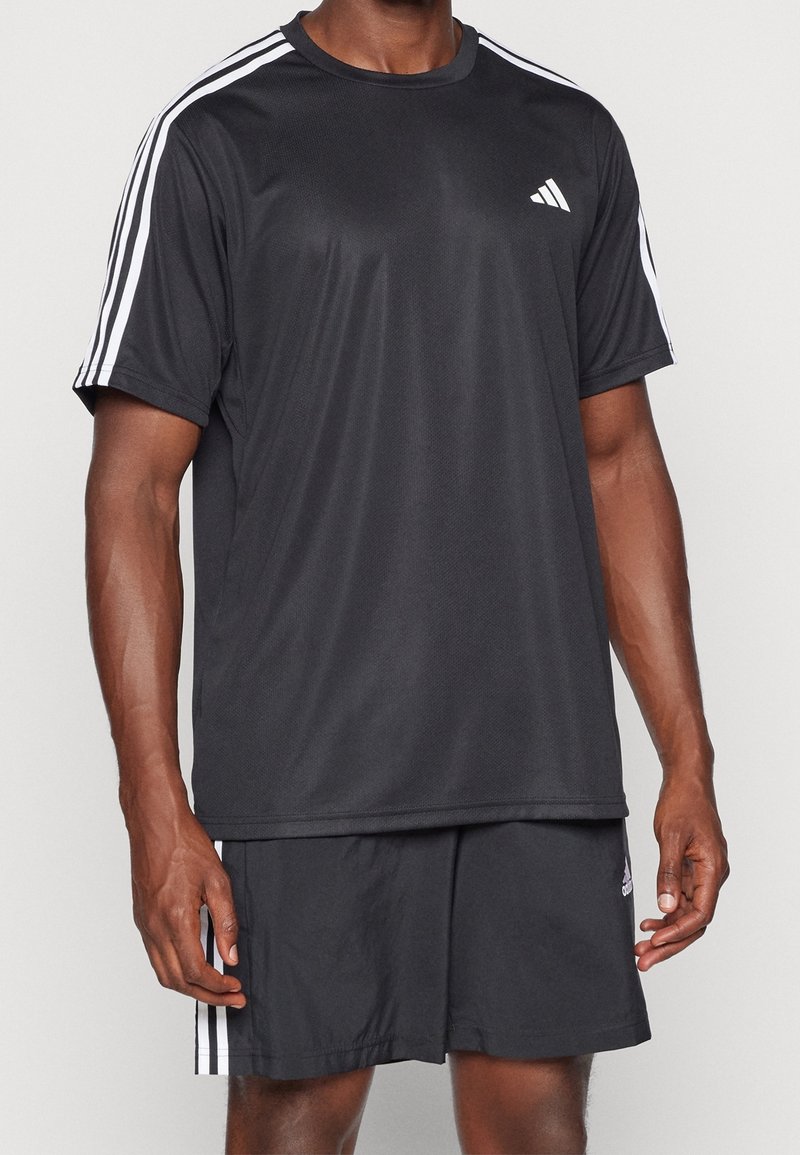 Černé sportovní tričko s bílými pruhy na ramenech, vyrobené z tkaniny odvádějící vlhkost. V páru s odpovídajícími černými šortkami se zvýrazněním loga.