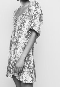 Kortärmad klänning med ormskinnstryck, djup V-urringning, rynkad front och flödande kjol. Tyget är lätt och har en mjuk textur.