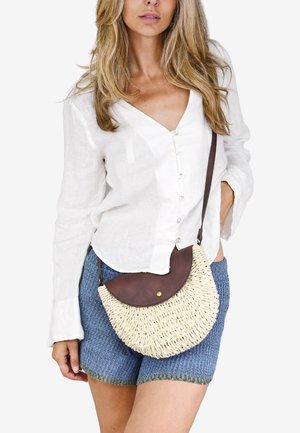 Bolso de mano redondo tejido de paja natural con una solapa de cuero marrón. Cuenta con una correa para el hombro y un cierre a presión.