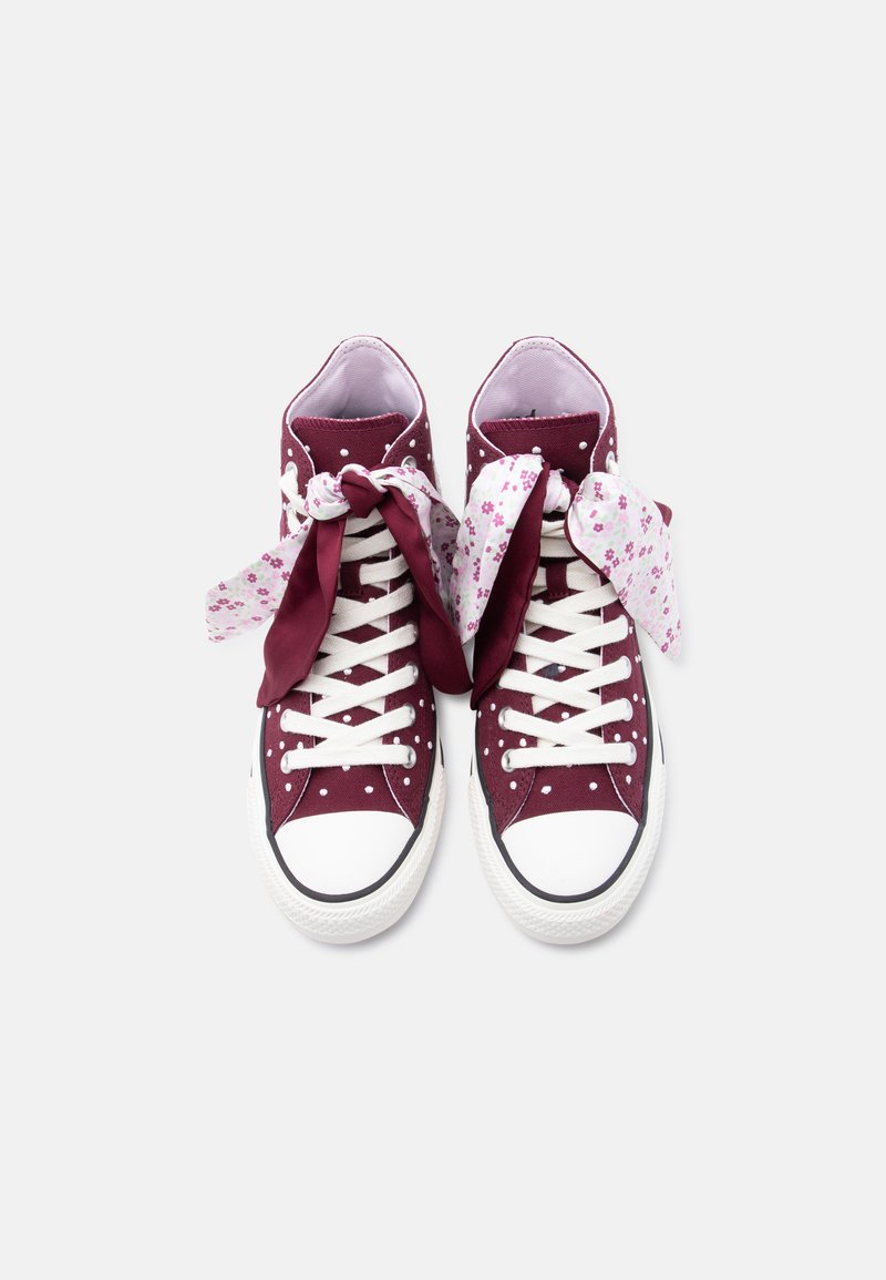 Sneakers alte color granata con pois, stringhe bianche e fiocchi di tessuto floreale annodati su sfondo bianco.