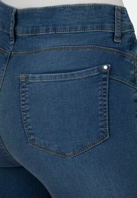 Dunkelblaue Jeans aus Denim mit einer Gesäßtasche, die einen kleinen silbernen Nieten hat, sichtbaren Nähdetails und einer glatten, leicht strukturierten Oberfläche.