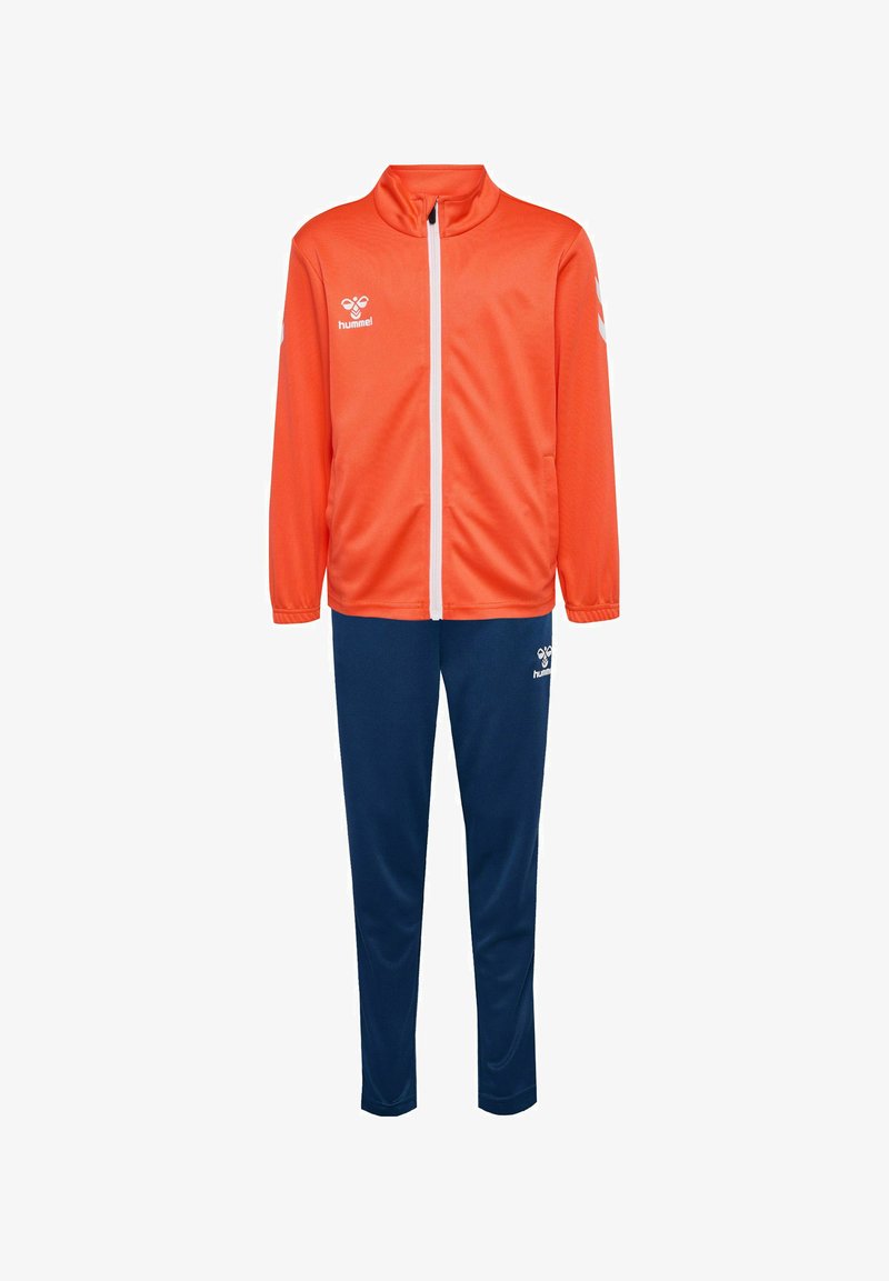 Veste de sport orange avec col haut et fermeture éclair blanche, assortie à un pantalon marine. Présente un logo sur les deux articles, fabriquée en tissu léger.