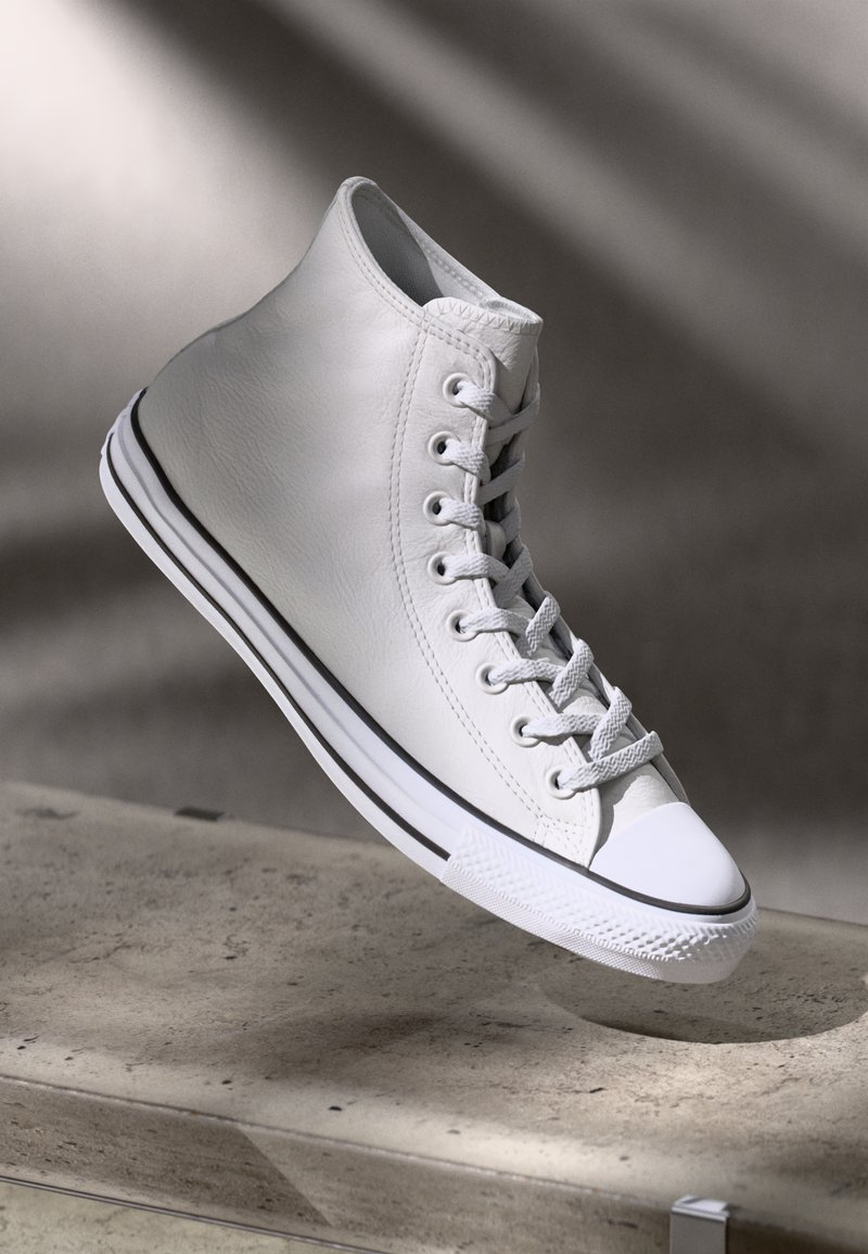 Hvit lær høy-topp sneakers med flate snøringer og gummisåle. Har en svart stripe langs bunnen og teksturerte detaljer rundt ankelen.