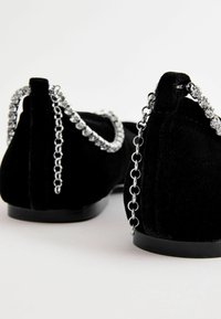 Zapatos de terciopelo negro con punta redonda, suela delgada negra y acento de cadena plateada con strass en la parte posterior.