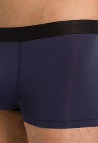 Mörkblå boxershorts i mjukt, stretchigt tyg med en svart midja som visar "HANRO"-logga. Slät textur och åtsittande design.